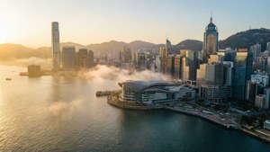 薄霧輕籠的維多利亞港日出，遠處帆影點綴，背景是高聳的香港天際線。