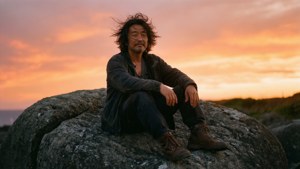 一個男人坐在石頭上，觀看海洋上充滿活力的日落。