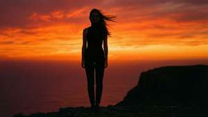 日落時分，一個女人站在懸崖上的剪影，風吹動她的頭髮