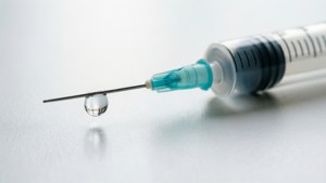 一個注射器，針頭掛著一滴液體，放在白色表面上。
