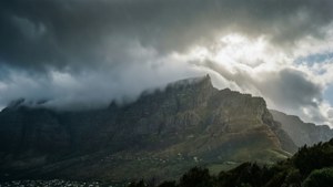 崎嶇的山峰穿過暴風雲聳立，陽光穿透雲層照耀在迷霧山谷之上。