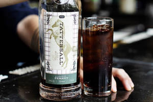 一瓶 Tattersall 利口酒和一杯加冰的深色汽水在吧檯上。