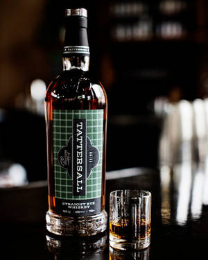 深色吧枱上的 Tattersall 純黑麥威士忌酒瓶和酒杯。