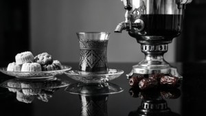 銀色茶壺、深色茶杯和一盤棗子糕點，置於反光表面上。