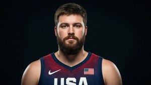 一位男性籃球運動員，身穿帶有美國國旗補丁的美國隊球衣，直視鏡頭。
