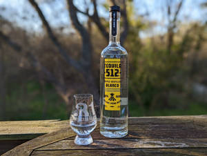 一瓶 512 Tequila Blanco 和品酒杯放在戶外的木桌上。