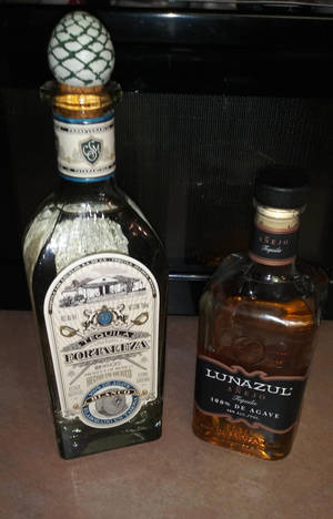 兩個龍舌蘭酒瓶，一個帶有菠蘿塞和華麗標籤，另一個帶有琥珀色液體和時尚黑色瓶蓋，並排放在枱面上。 — Honor Pad 20 Pro 壁紙