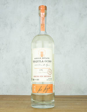 一瓶Tequila Ocho reposado放在木頭上，背景是灰色牆壁。