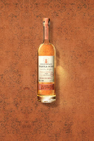 一瓶 El Patrón Tequila Ocho 放在帶有紋理的陶土表面上。