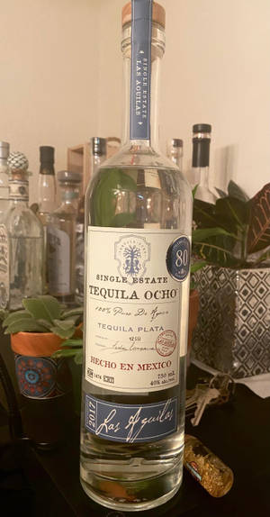一瓶Las Aguilas龍舌蘭酒放在桌子上，旁邊有其他瓶子和植物。