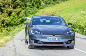 在陽光明媚的日子裡，一輛灰色 Tesla Model S 在蜿蜒的道路上行駛，穿過綠色的山丘。