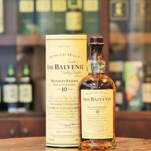 木製吧枱上的一瓶Balvenie Founder's Reserve威士忌及盒子，後面是其他酒瓶架。