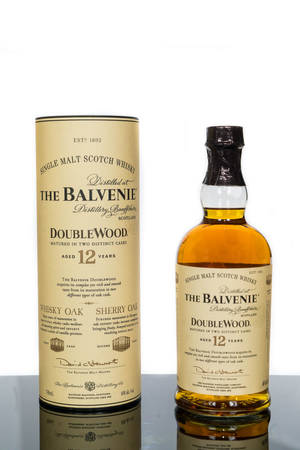 一瓶Balvenie 12 Year Old DoubleWood威士忌及其盒子，置於反光表面上。