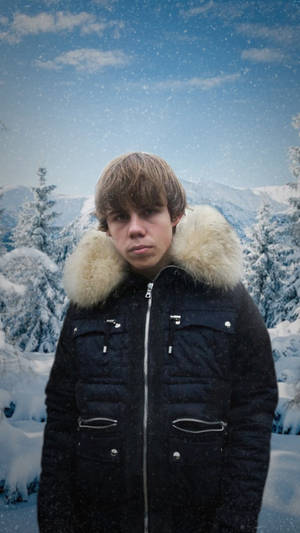 年輕男子穿著冬季外套站在雪地山林中