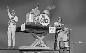 The Kinks 樂隊在剪刀升降台上現場演奏，配有結他和鼓。 — 復古 壁紙