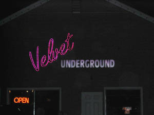 黑暗建築物上的 Velvet Underground 霓虹燈牌，窗戶裡亮著營業中的標誌。