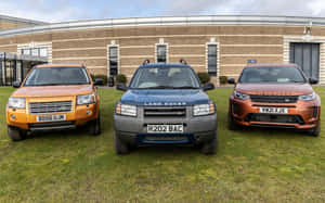 三輛 Land Rover SUV 停泊在現代磚砌建築前的草地上。 — Steam Deck OLED 壁紙