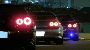 三輛跑車在夜間停放在工業區，尾燈發出光芒。