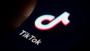 手指靠近黑暗手機屏幕上發光的TikTok應用程式標誌。