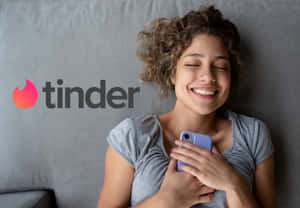 女性在灰色沙發上拿著手機微笑，Tinder 標誌可見