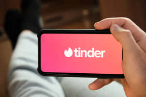 手拿著手機，在粉紅色屏幕上顯示Tinder應用程式標誌。