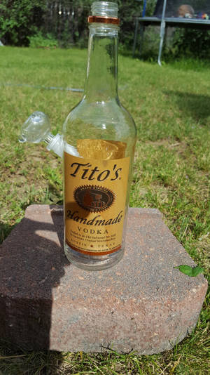 Tito's伏特加酒瓶與水煙槍配件，放在草地上的磚上。