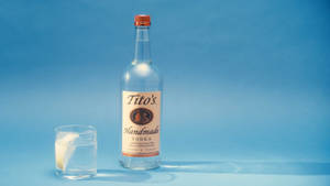 Tito's伏特加酒瓶和裝有冰塊和檸檬的玻璃杯，藍色背景