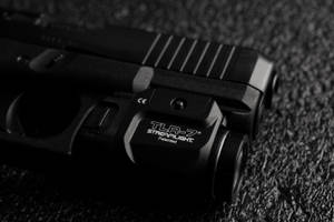 黑色手槍配備 Streamlight TLR-7 激光瞄準器，置於紋理表面。