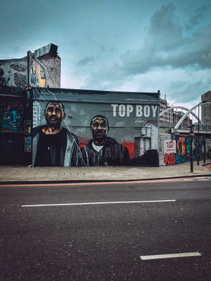 陰天下城市建築物上的《Top Boy》角色街頭壁畫。