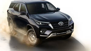 黑色豐田 Fortuner SUV 在攝影棚環境中向前行駛，揚起灰塵雲。 — 汽車 壁紙