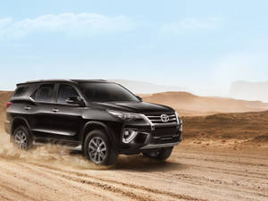 黑色豐田 Fortuner SUV 在沙漠地形上行駛，揚起沙塵。