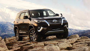 黑色豐田 Fortuner SUV 在岩石山地地形上，背景有山脈。