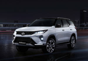 銀色豐田 Land Cruiser Legend SUV 在夜間濕滑的城市道路上，車頭燈和城市燈光閃爍。