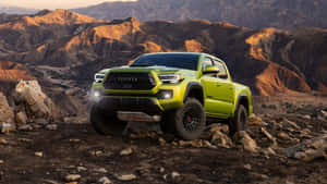 青檸綠色豐田 Tacoma 皮卡車停在岩石沙漠地形上，背景有山脈。 — 汽車 4K 壁紙