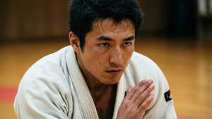 一位男性柔道運動員穿著白色柔道服在道場中雙手合十跪著