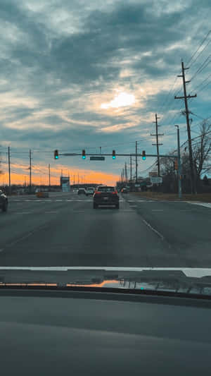從汽車擋風玻璃看日落時交通燈的景色，有橙色雲朵和電線