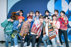 K-pop 團體在藍色幾何牆前穿著色彩繽紛的街頭服飾擺姿勢。 — 角落生物 壁紙