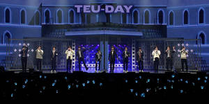 K-pop組合在藍色燈光舞台上表演，粉絲們舉著發光的燈光。