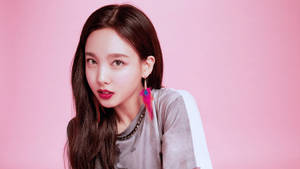 年輕女性，長長的黑髮和彩色羽毛耳環，穿著灰色T恤，粉紅色背景。