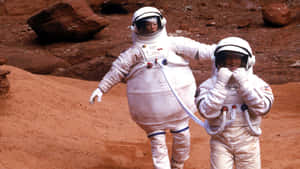 兩名身穿白色太空衣的太空人正在探索紅色岩石行星表面。 — 太空人 壁紙