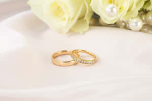 兩枚金色結婚戒指，配以珍珠和黃色玫瑰，置於白色布料上。