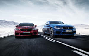 黃昏時分，兩輛紅色和藍色BMW M5在積雪的山路上飛馳。 — Steam Deck OLED 壁紙