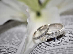 兩枚結婚戒指放在打開的書上，旁邊有一朵白百合。
