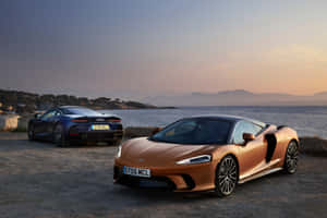 兩輛McLaren跑車在日落時停泊在懸崖上，享有海景。 — Surface Pro 壁紙
