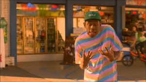身穿條紋襯衫和帽子的男子在日落時於店外做出表情豐富的臉 — Tyler the creator GIF 壁紙