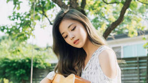 年輕女性在陽光下樹蔭中抱著結他