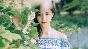 身穿藍色上衣的年輕女性，在花園中從開花的綠色枝條間探出頭來。