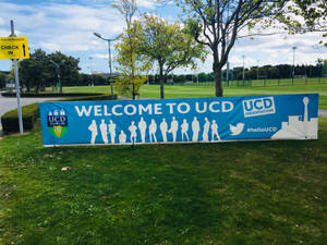 UCD歡迎橫幅，草地上有學生剪影，靠近校園建築。