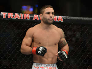 一位赤裸上身的MMA拳手戴著UFC手套站在籠內。