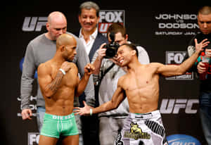 兩名男性UFC拳手在稱重活動中擺姿勢，身後有相機和品牌橫幅。